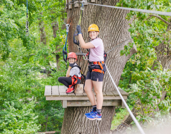 Drei Kinder mit Helm klettern gesichert in einem Kletterelement