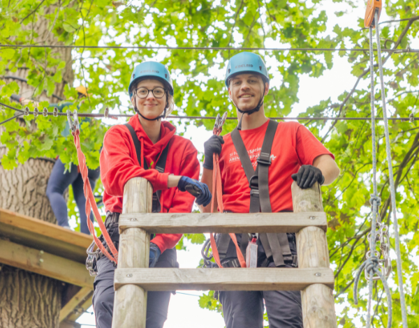 Zwei Guides, die in die Kamera lcheln, whrend sie auf einem Kletterelement stehen
