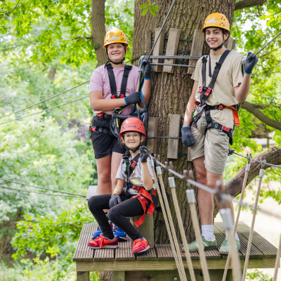 Drei Kinder mit Helm klettern gesichert in einem Kletterelement